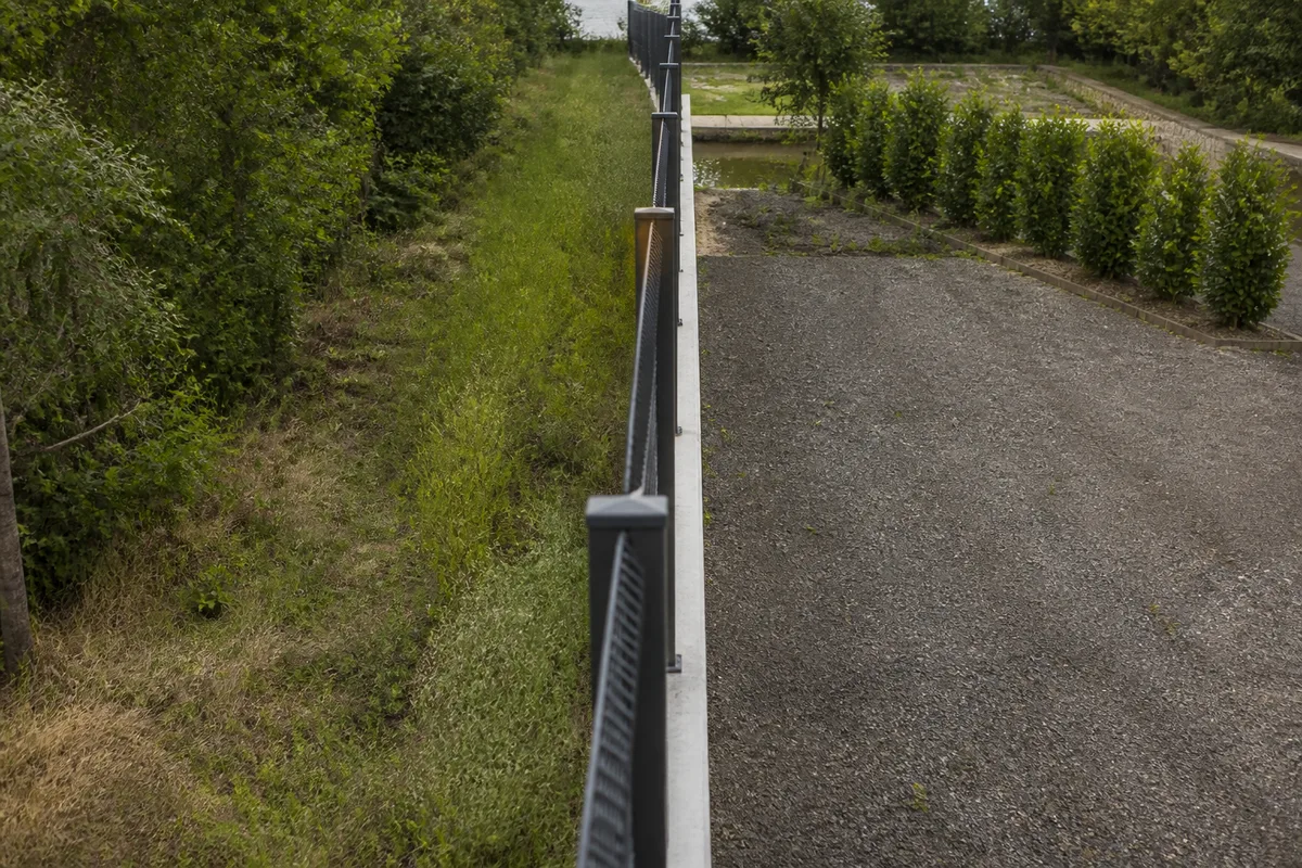 Ligne de clôture rigide rehaussée vue dans son axe, poteaux alignés au cordeau